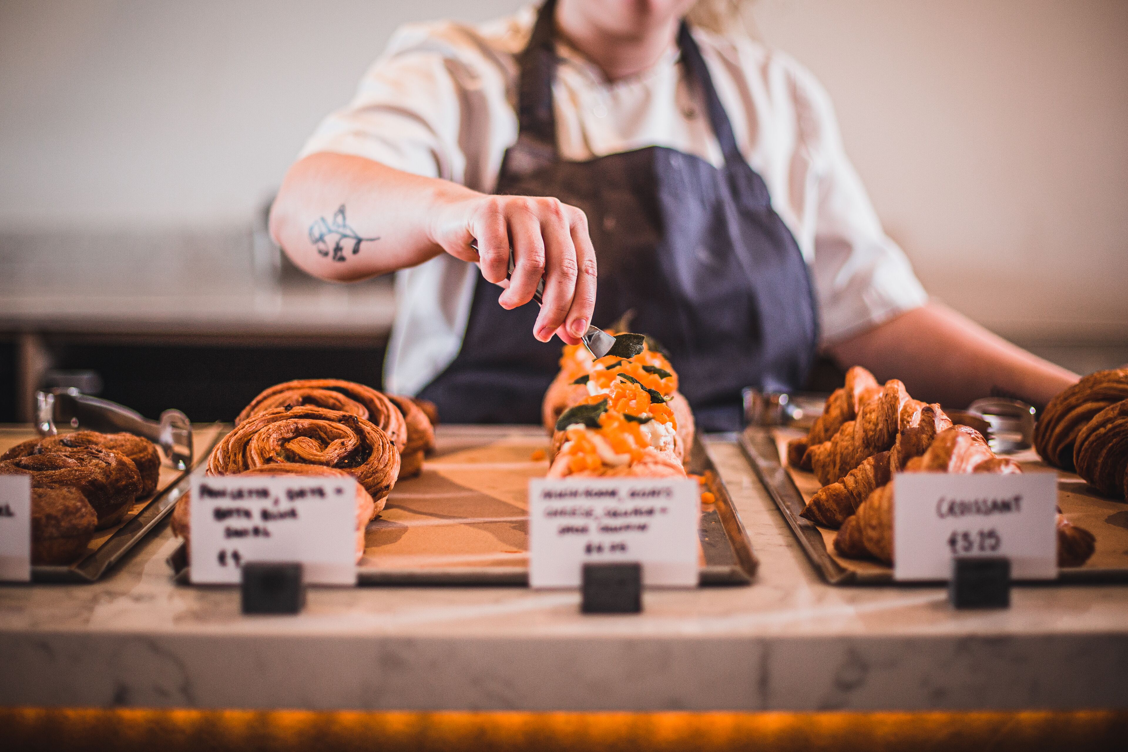A bakery counter with various pastries and a person arranging them.