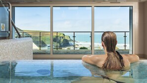 A person relaxing in a glass-bottomed hot tub with a view of the ocean and cliffs. - Bedruthan Hotel and Spa (Newquay)