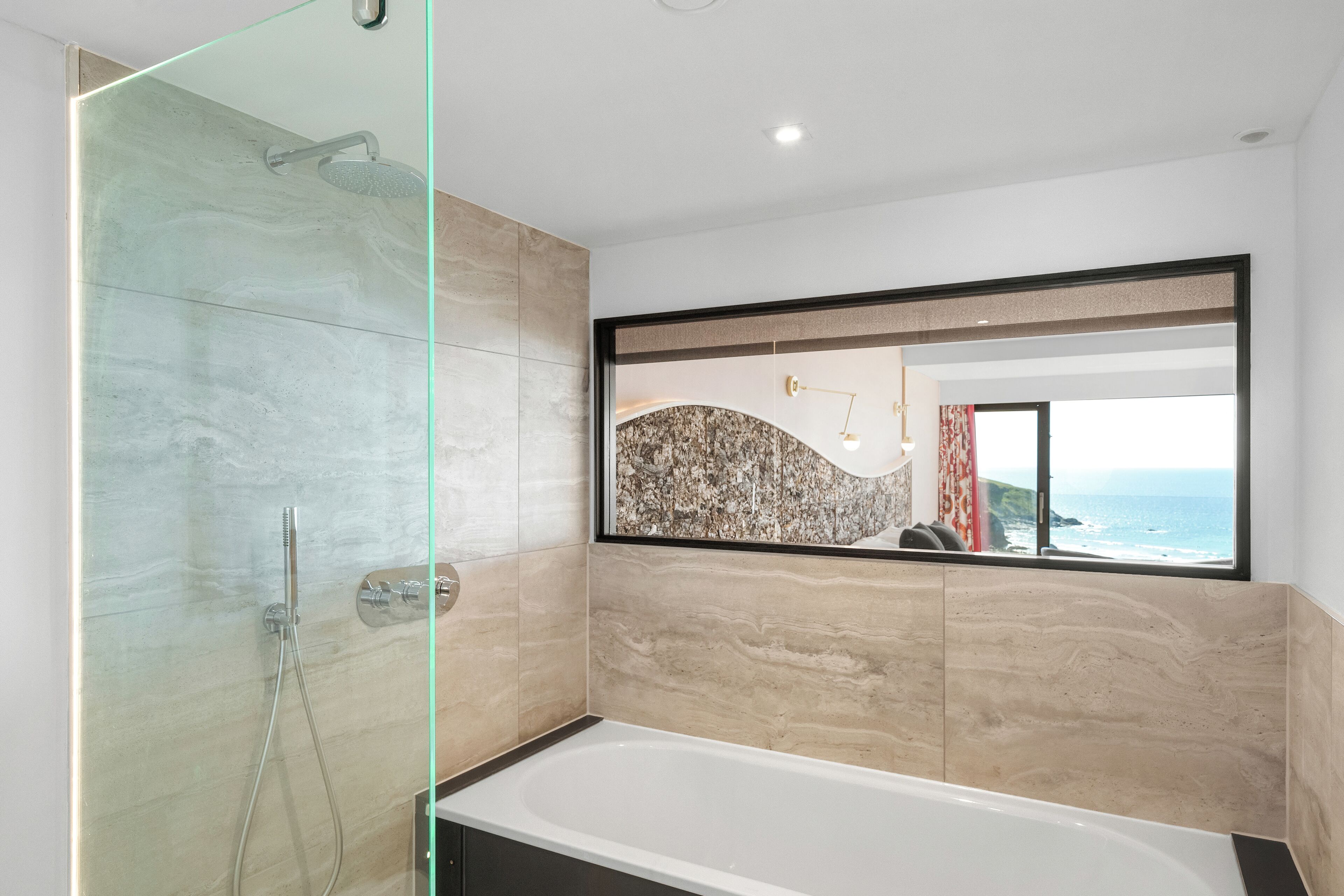 A modern bathroom with a glass-enclosed shower, a large bathtub, and a view of the ocean through a window.
