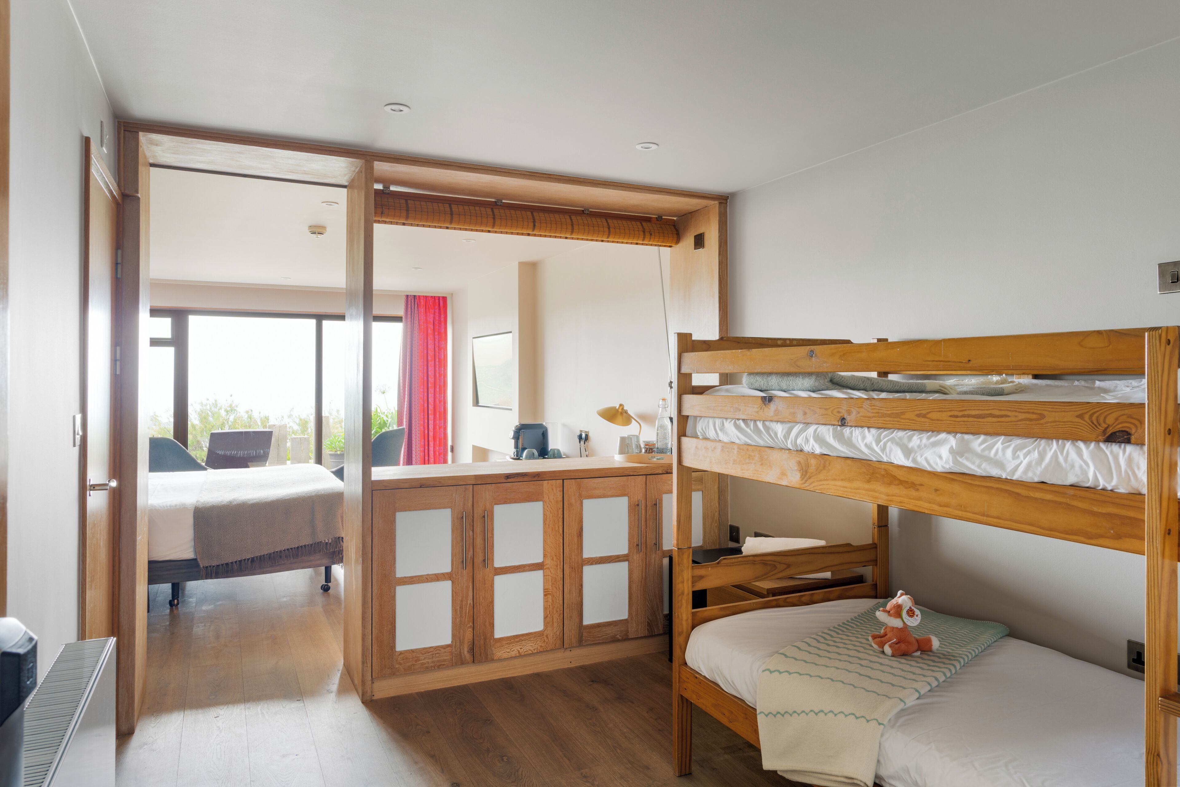Una habitación con literas, armarios de madera, un escritorio y vistas por una puerta abierta.