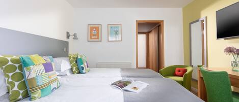 Ein Hotelzimmer mit zwei Betten, einem Schreibtisch, einem Stuhl, einem Fernseher und zwei gerahmten Bildern an der Wand.