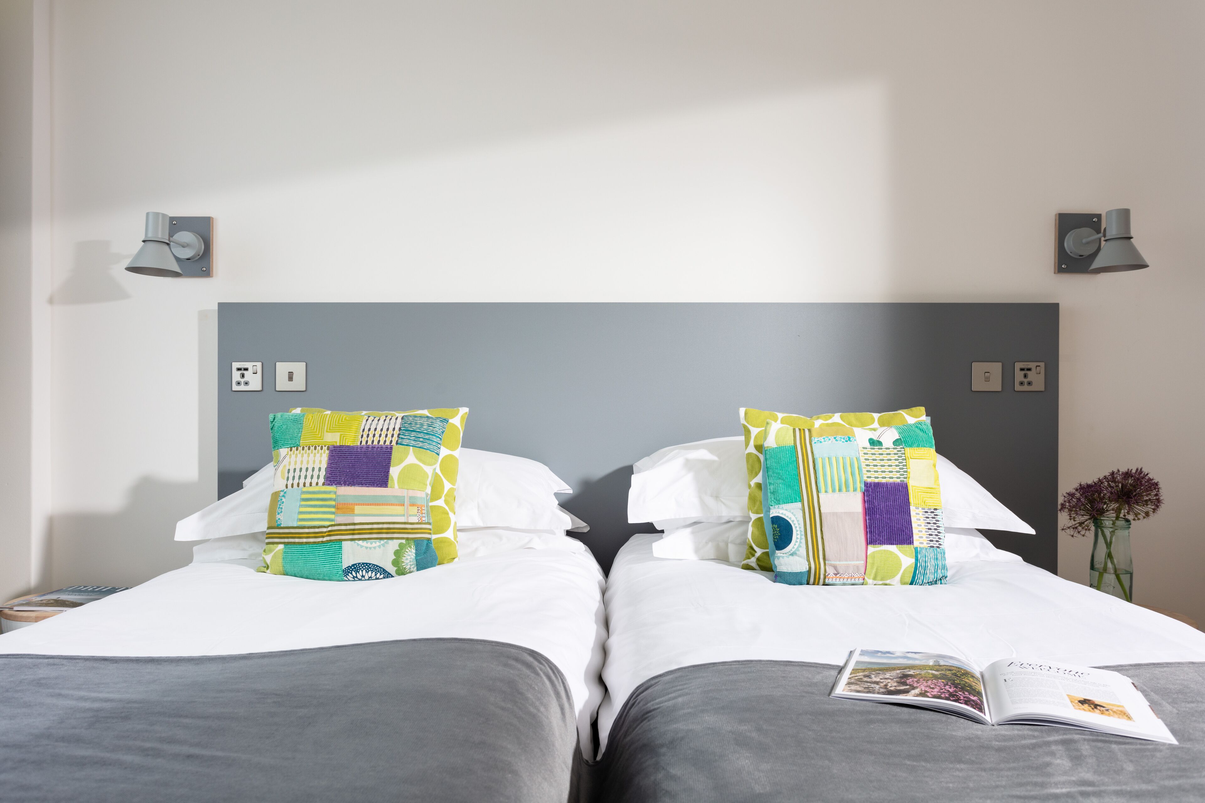 A double bed with a gray headboard, two bedside tables, and a book on the bed.