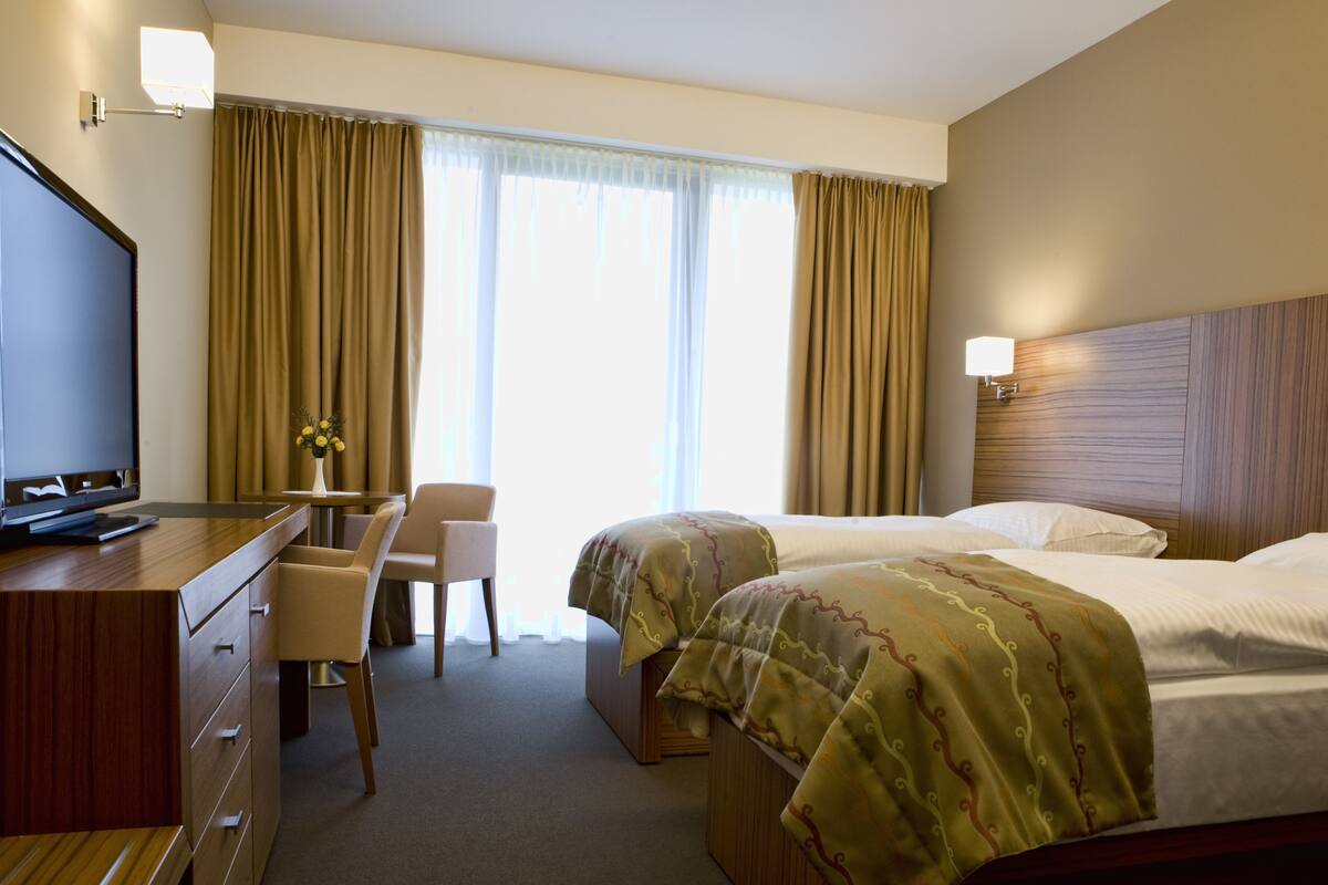Une chambre d’hôtel équipée d’un bureau, de deux lits, d’une télévision et d’une fenêtre avec des rideaux.