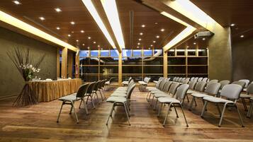 A conference room with rows of chairs, a long table with a microphone, and large windows with a view of the mountains.