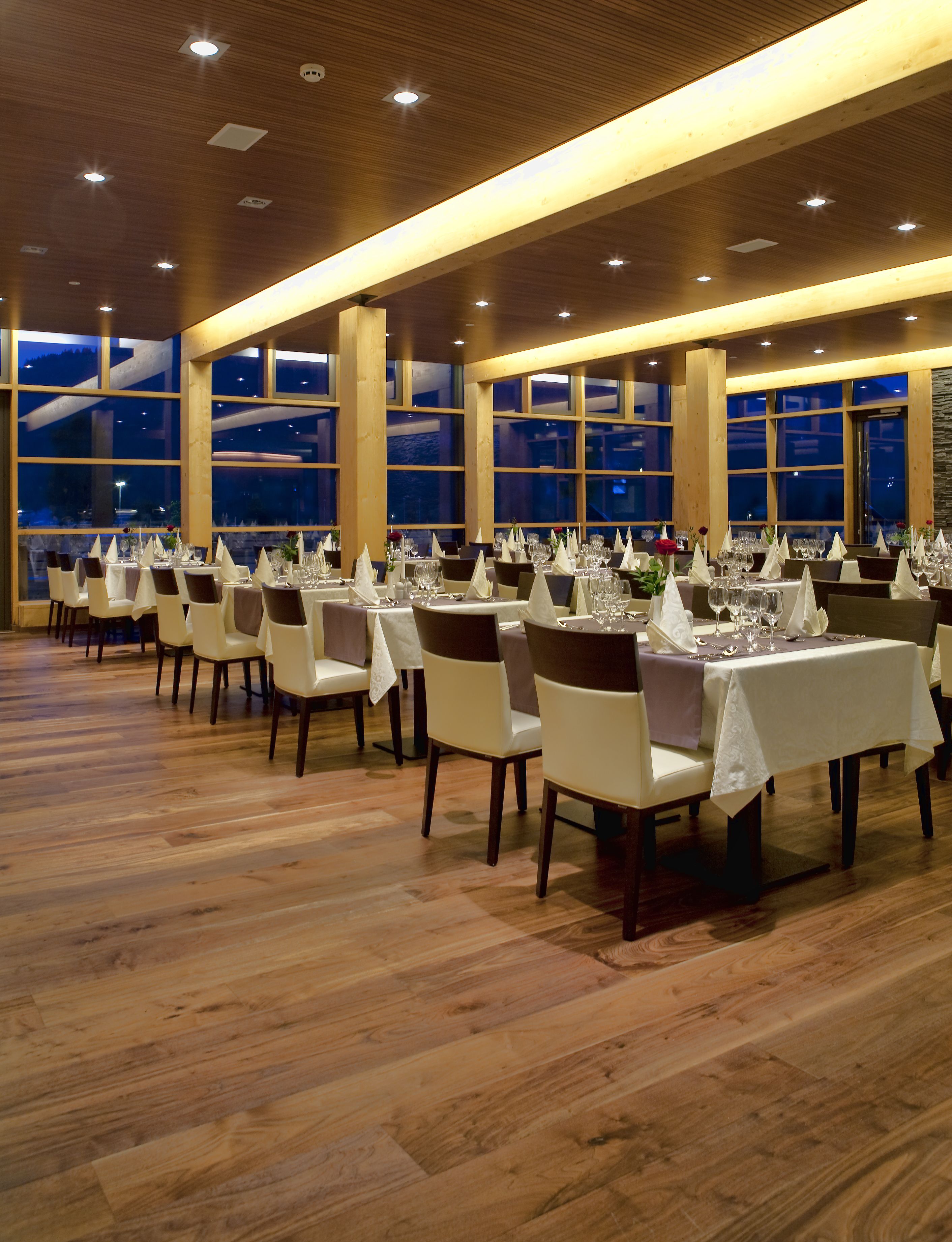 Een restaurant met meerdere tafels gedekt voor diners, grote ramen en een houten vloer.