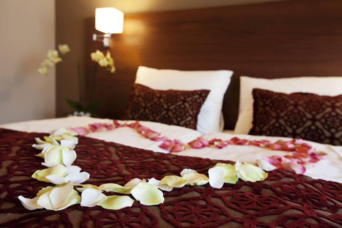 Un lit bien fait, avec une couvre-lit à motifs, deux oreillers et une guirlande décorative de fleurs.