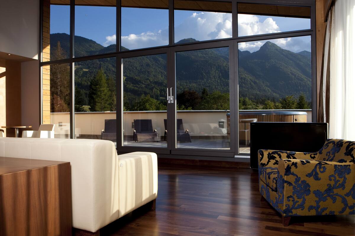 Une chambre moderne dotée d’une grande fenêtre offrant une vue sur les montagnes, d’un plancher en bois et d’un canapé recouvert d’un tissu à motifs.