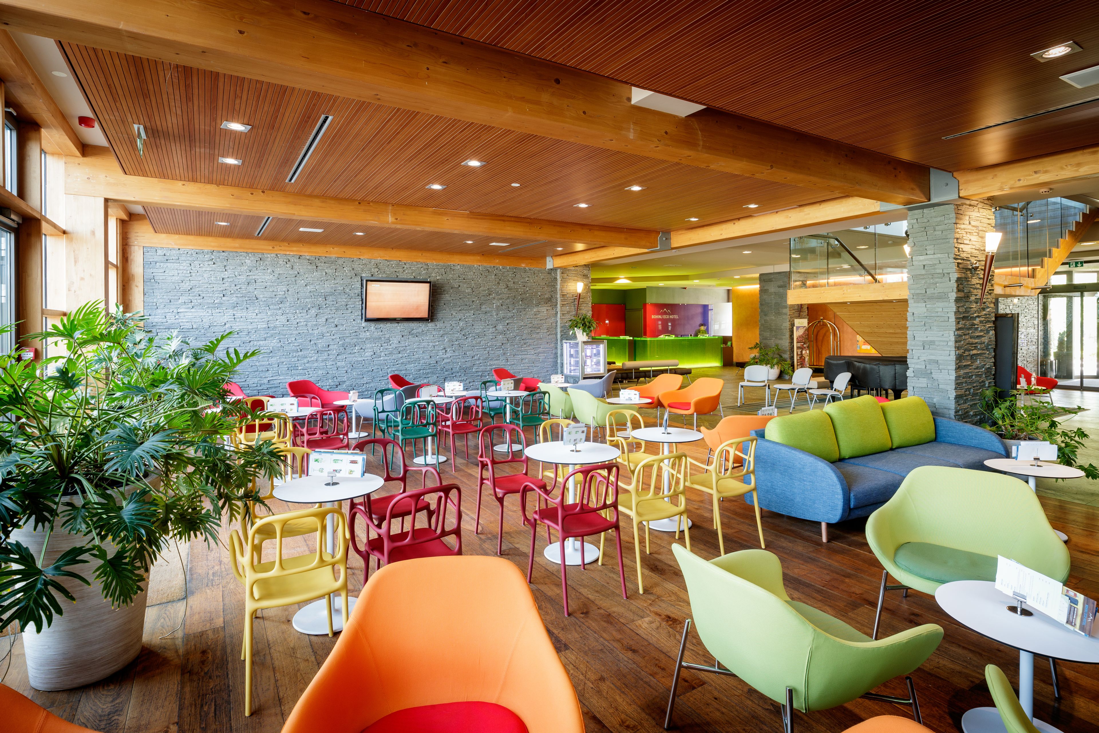 A modern indoor space with wooden ceilings, colorful seating, and a stone wall.