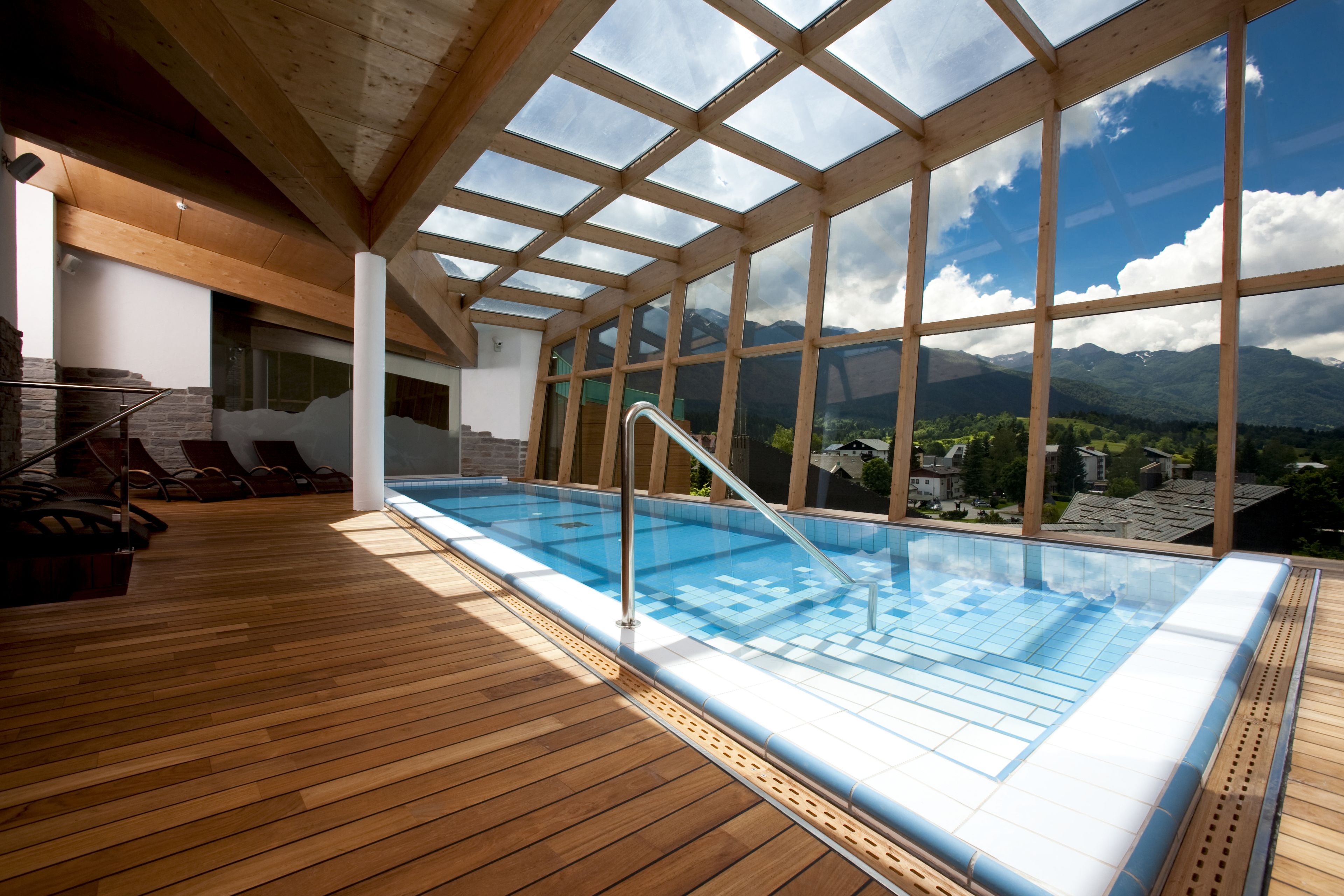 An indoor swimming pool with a wooden deck, large windows, and a view of mountains.