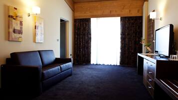 Une chambre d’hôtel avec une moquette sombre, un canapé en cuir, un bureau avec un téléviseur à écran plat et deux lampes fixées au mur.