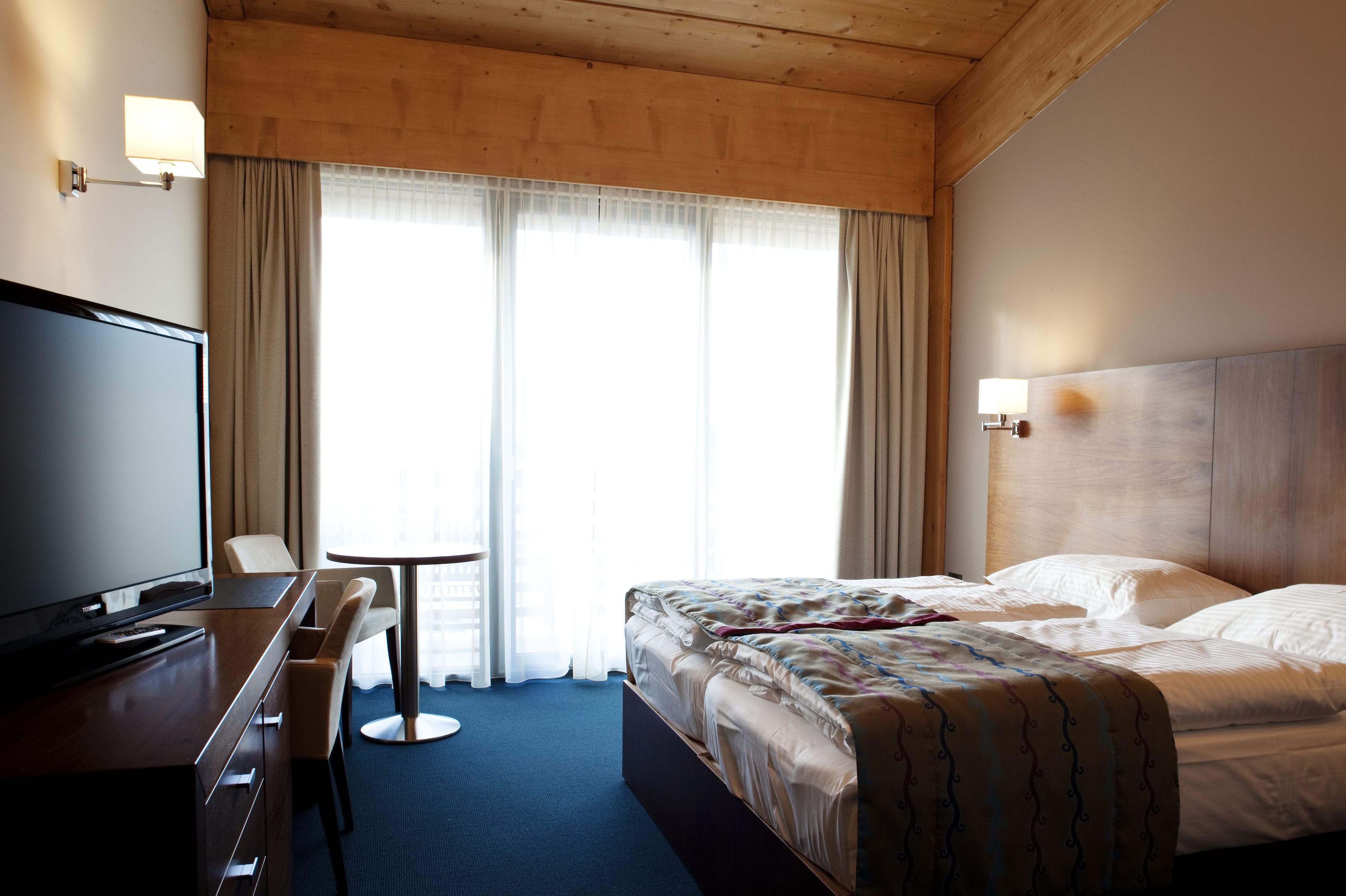 A hotel room with a bed, a desk with a chair, a television, and a window with curtains.