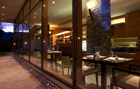 Un espace repas moderne agrémenté d’une colonne en pierre, de murs en verre et offrant une vue sur les montagnes.
