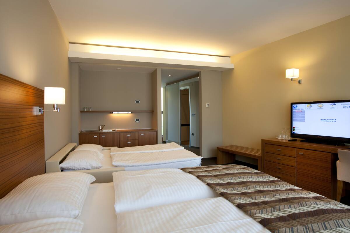 Une chambre d’hôtel avec trois lits, une télévision, un bureau et une salle de bain visible à travers une porte ouverte.