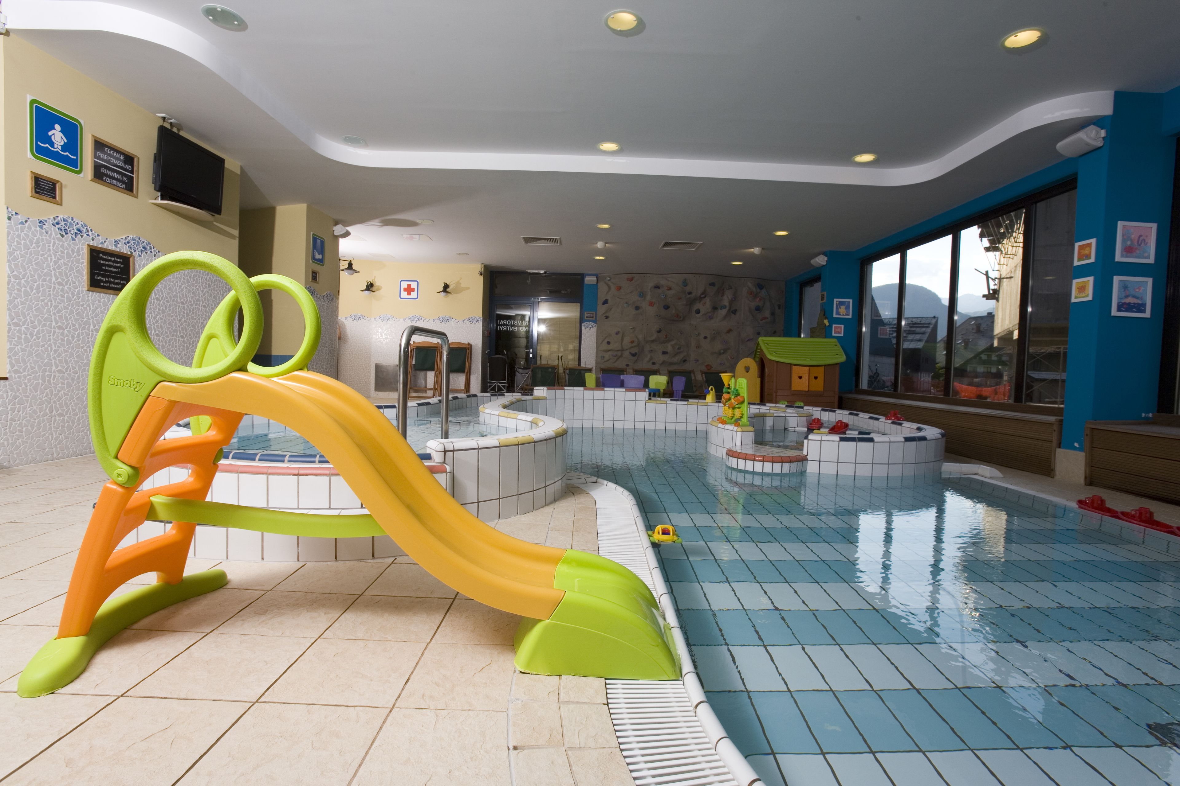 An indoor swimming pool with a slide, a play area, and a lifeguard station.