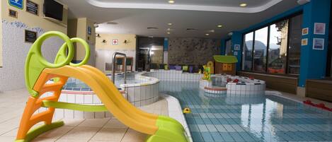 An indoor swimming pool with a slide, a play area, and a lifeguard station.