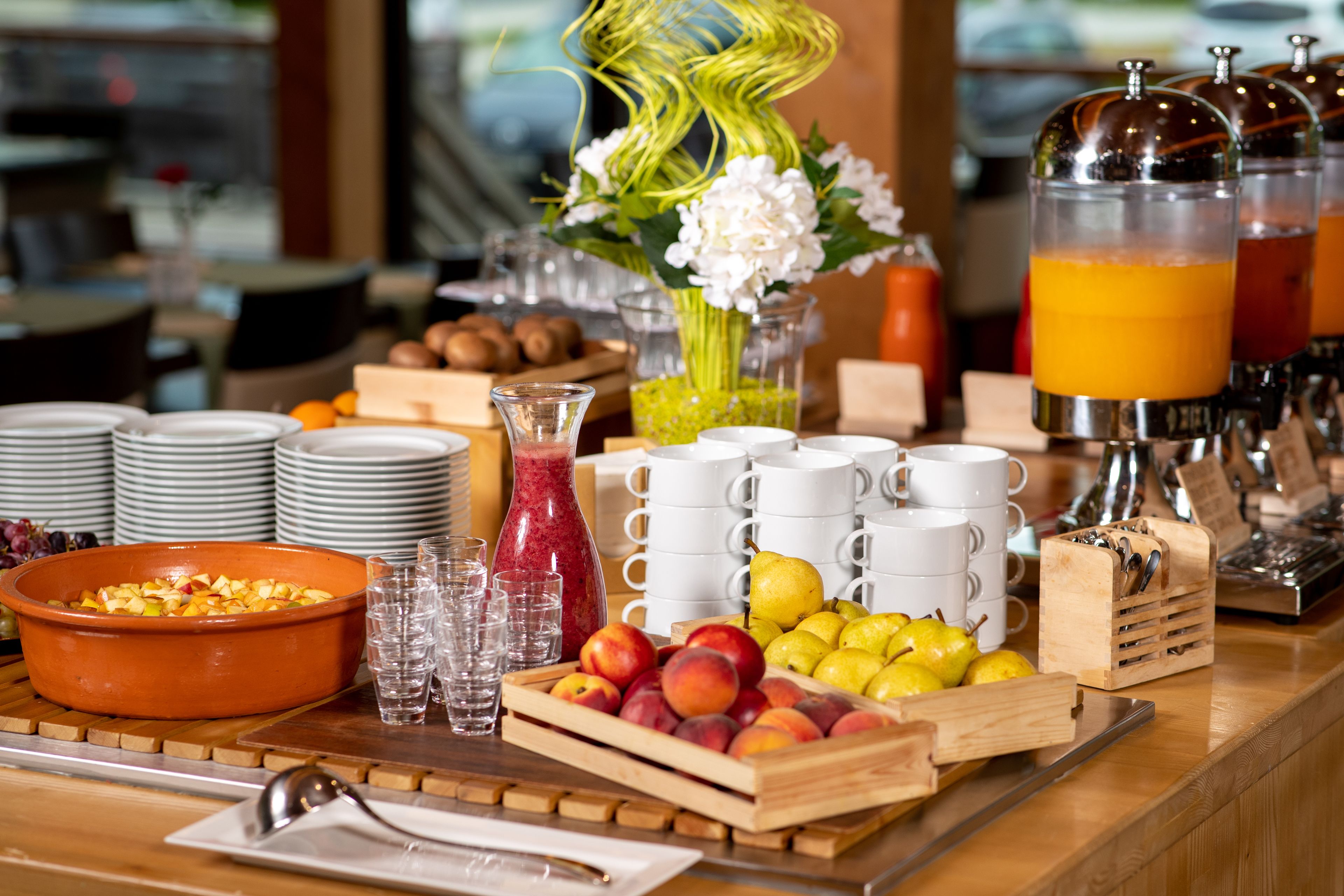 A breakfast buffet with fruits, juices, and coffee mugs.
