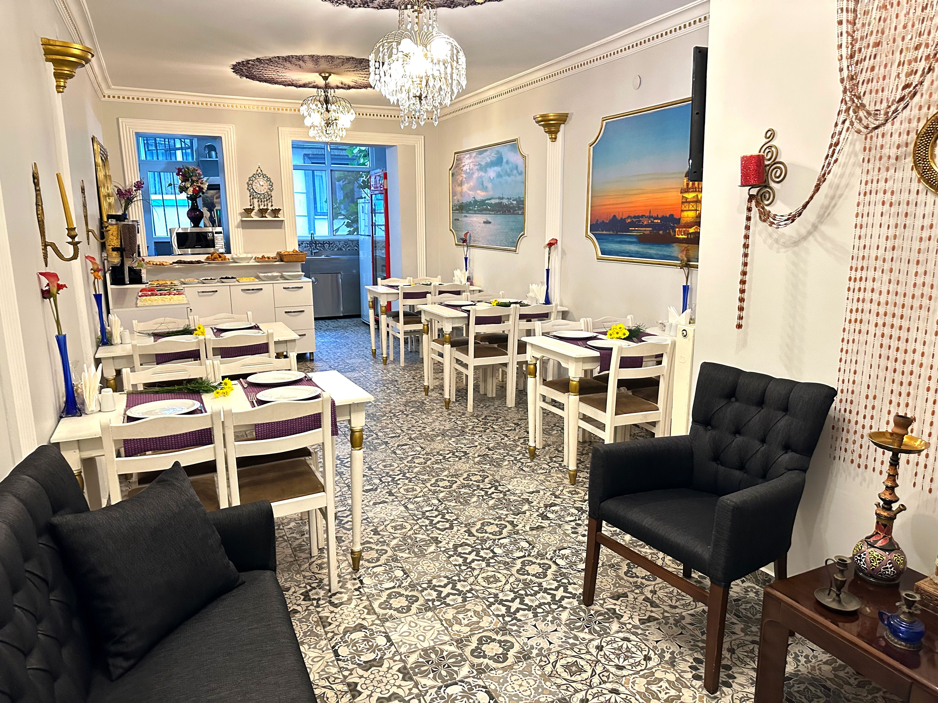 A dining area with white tables and chairs, a black sofa, and a chandelier.