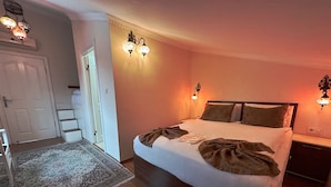 Une chambre avec un grand lit, un plancher en bois, un tapis à motifs et des lampes fixées au mur.