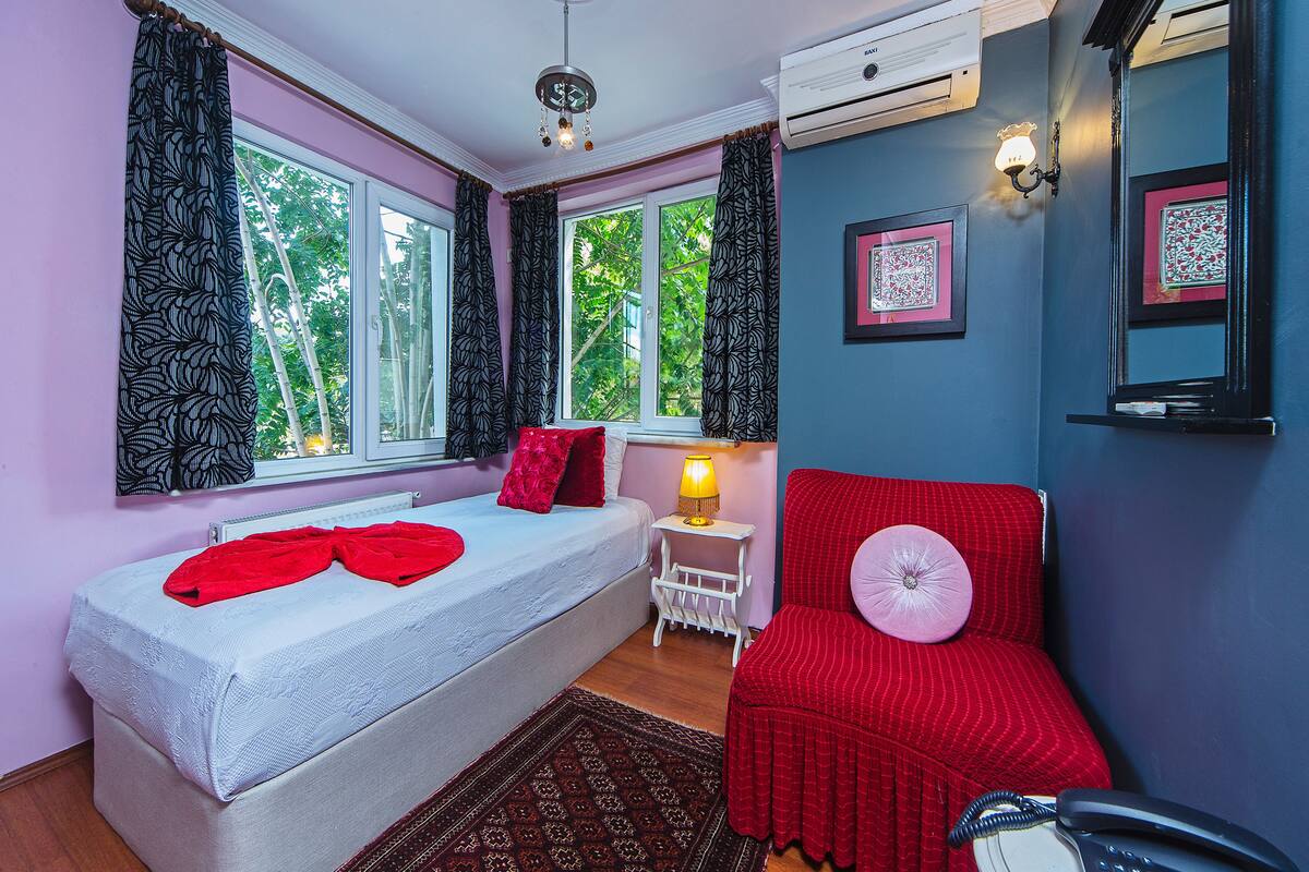 Une chambre à coucher avec un lit, une chaise rouge, une table de chevet avec une lampe et une fenêtre avec des rideaux.