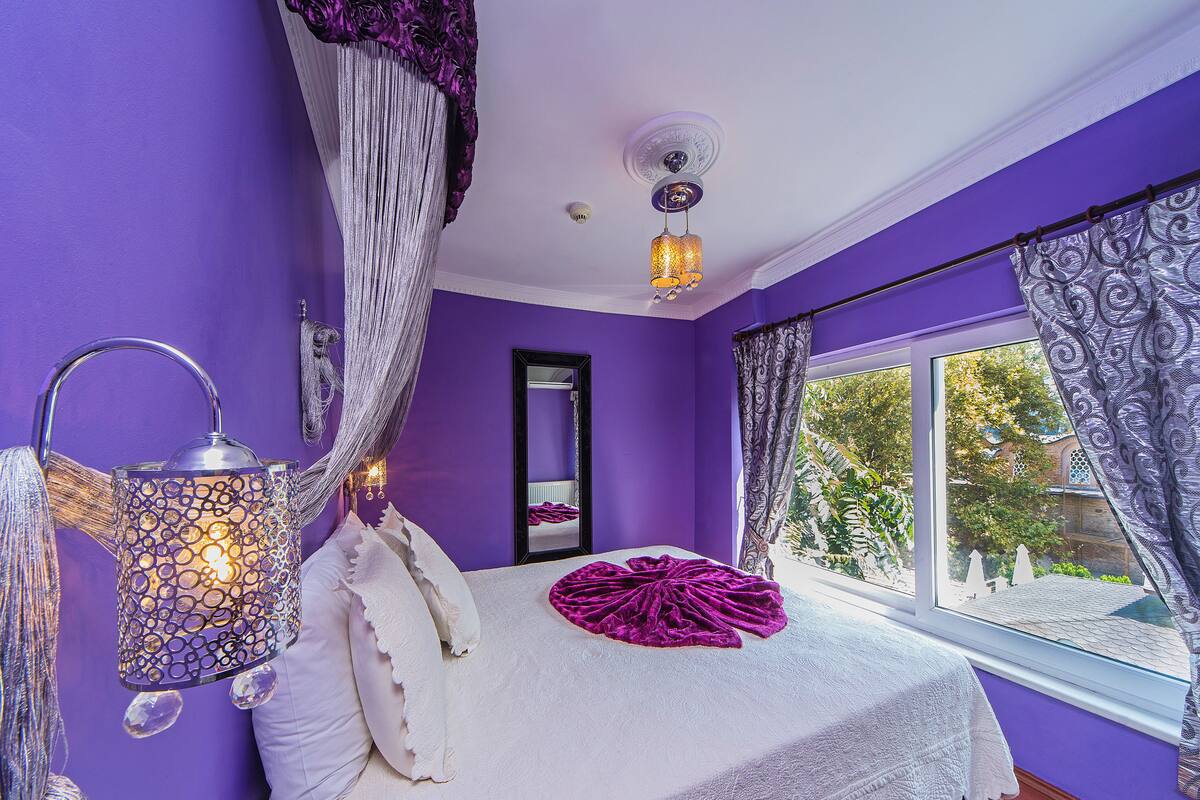 Une chambre à coucher avec un grand lit, un baldaquin, une table de chevet avec une lampe et une fenêtre avec des rideaux.