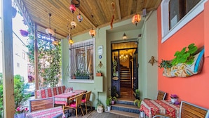 Une terrasse en bois avec des sièges extérieurs, un escalier menant à l’intérieur et des guirlandes lumineuses décoratives suspendues.