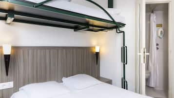 A hotel room with a bunk bed, bedside lamps, a wooden headboard, and a visible bathroom with a shower.