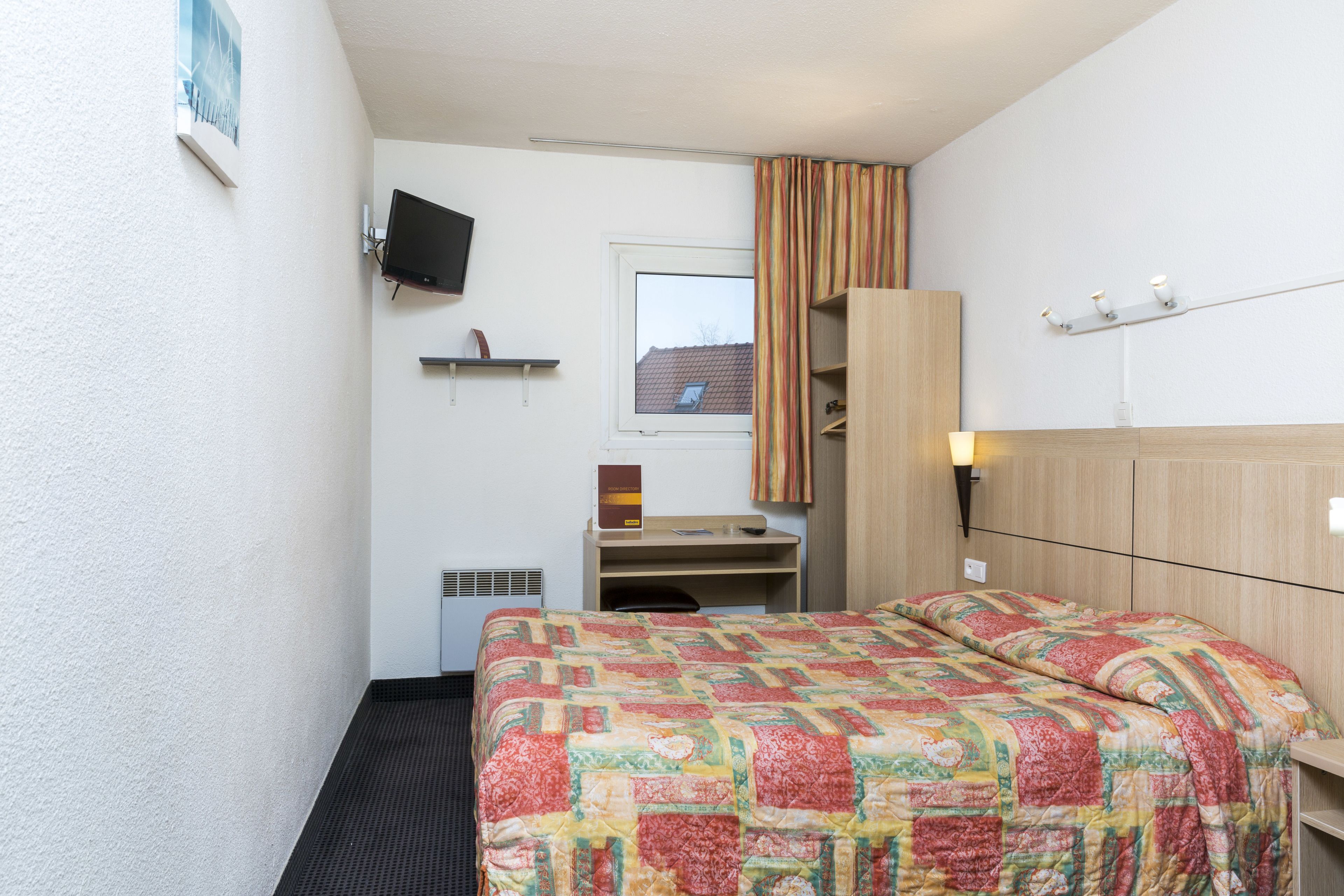 A hotel room with a bed, a desk, a chair, a television, a window, and a curtain.