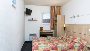 Habitación de hotel con cama, escritorio, silla, televisor, ventana y cortina.