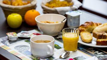 Una mesa de desayuno con un periódico, una taza de café, un vaso de jugo de naranja, un tazón de cereal, un croissant y una cesta de fruta.