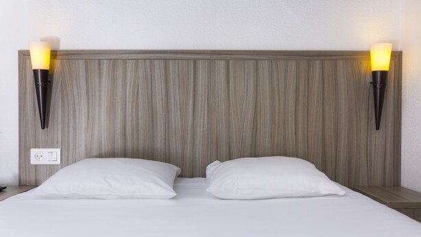 Una cama con sábanas blancas y dos mesitas de noche, cada una con una lámpara de pared.