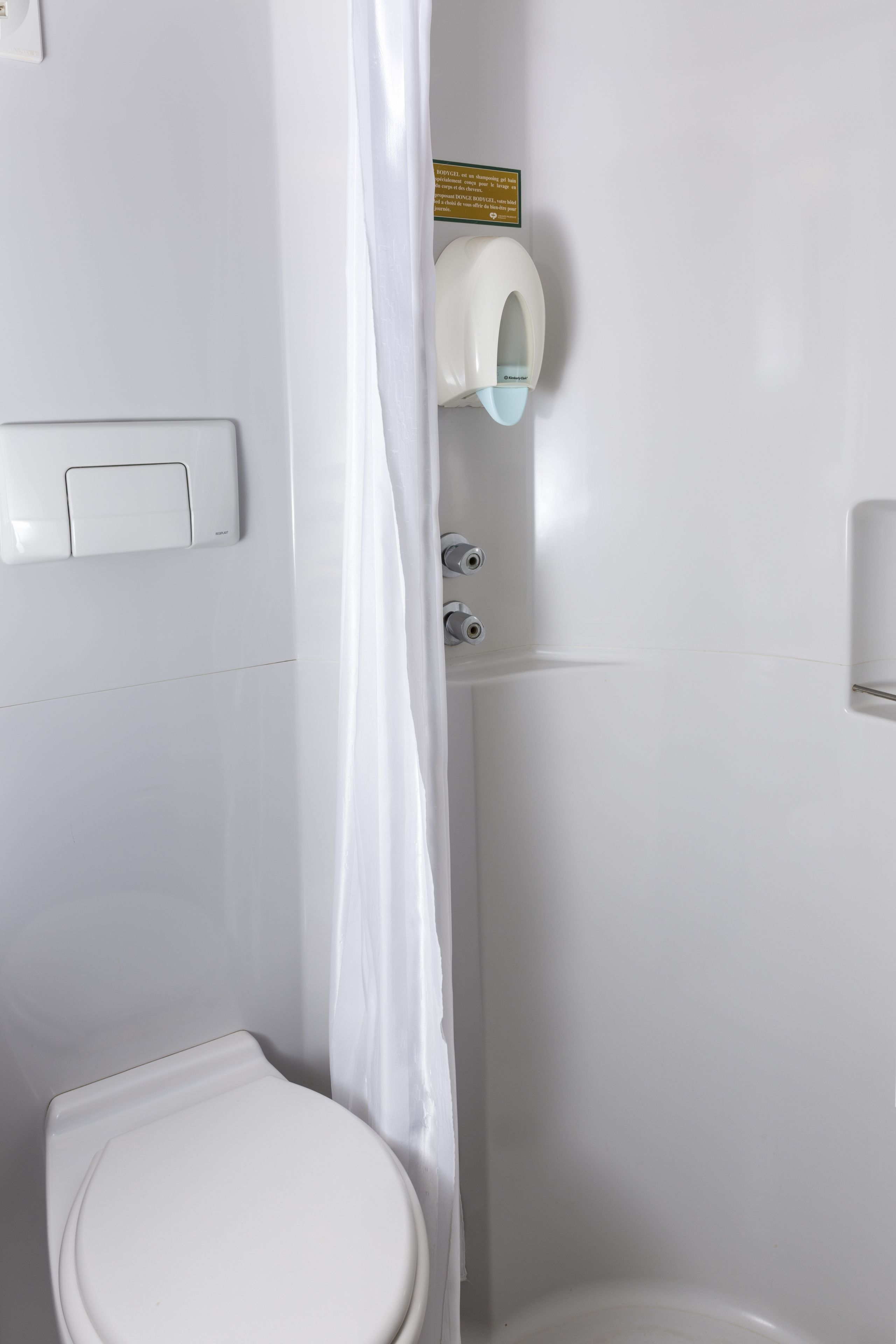 A white toilet with a paper towel dispenser mounted on the wall.