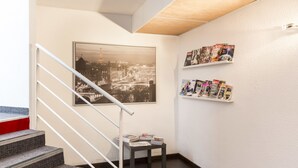 Una escalera con barandilla, una fotografía enmarco de un paisaje urbano y una pequeña mesa con revistas.