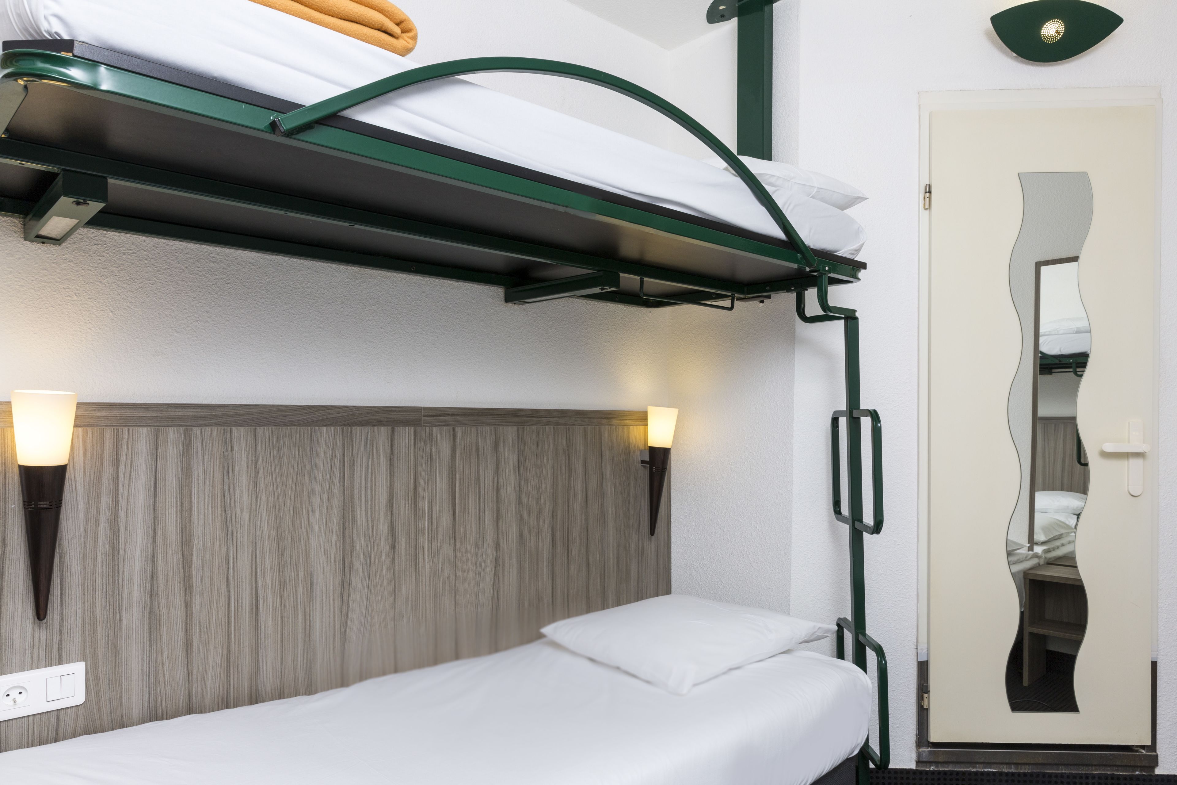 A bunk bed with a headboard, two bedside lamps, and a mirror on the door.