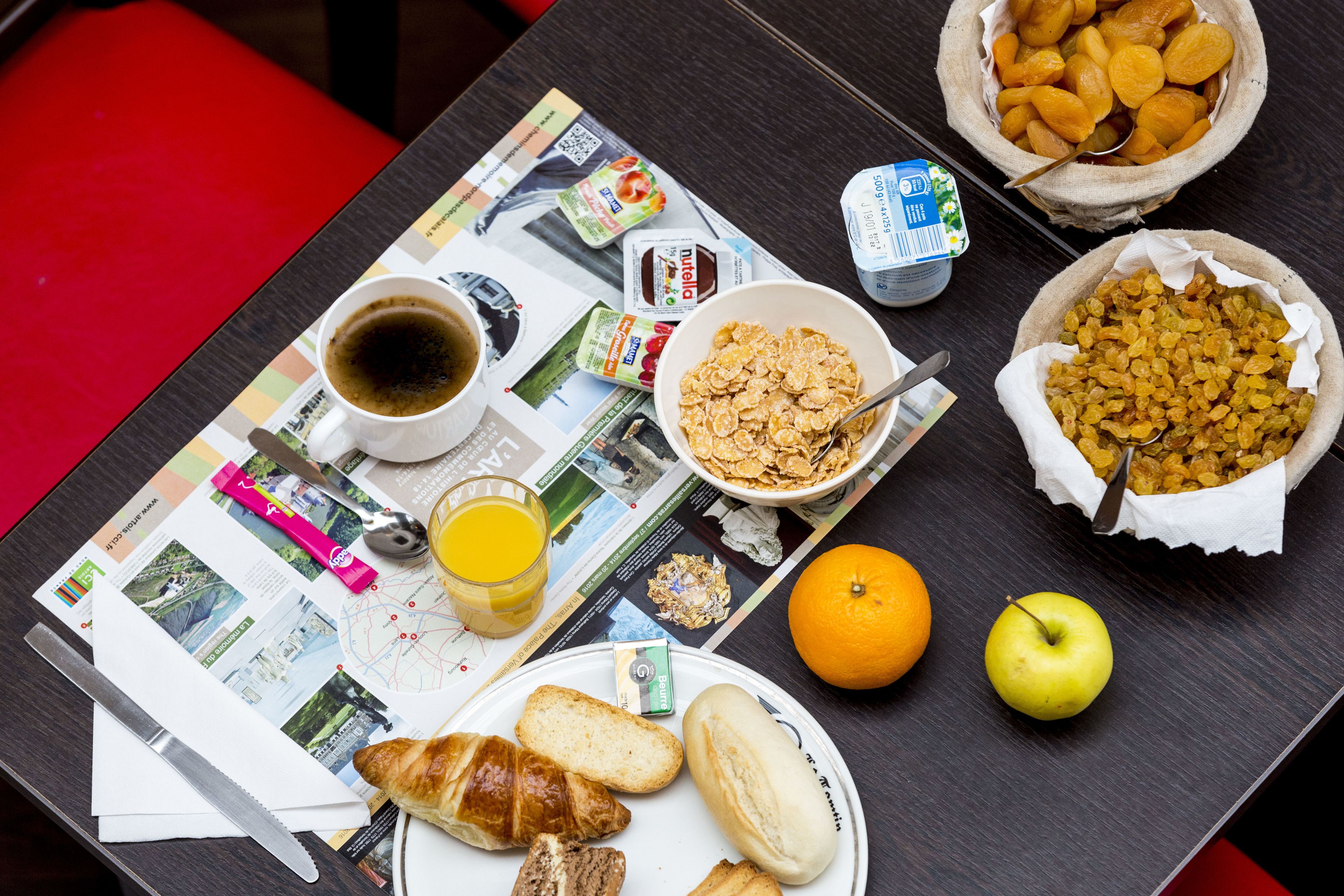 A breakfast table with croissants, orange juice, cereal, and a newspaper.