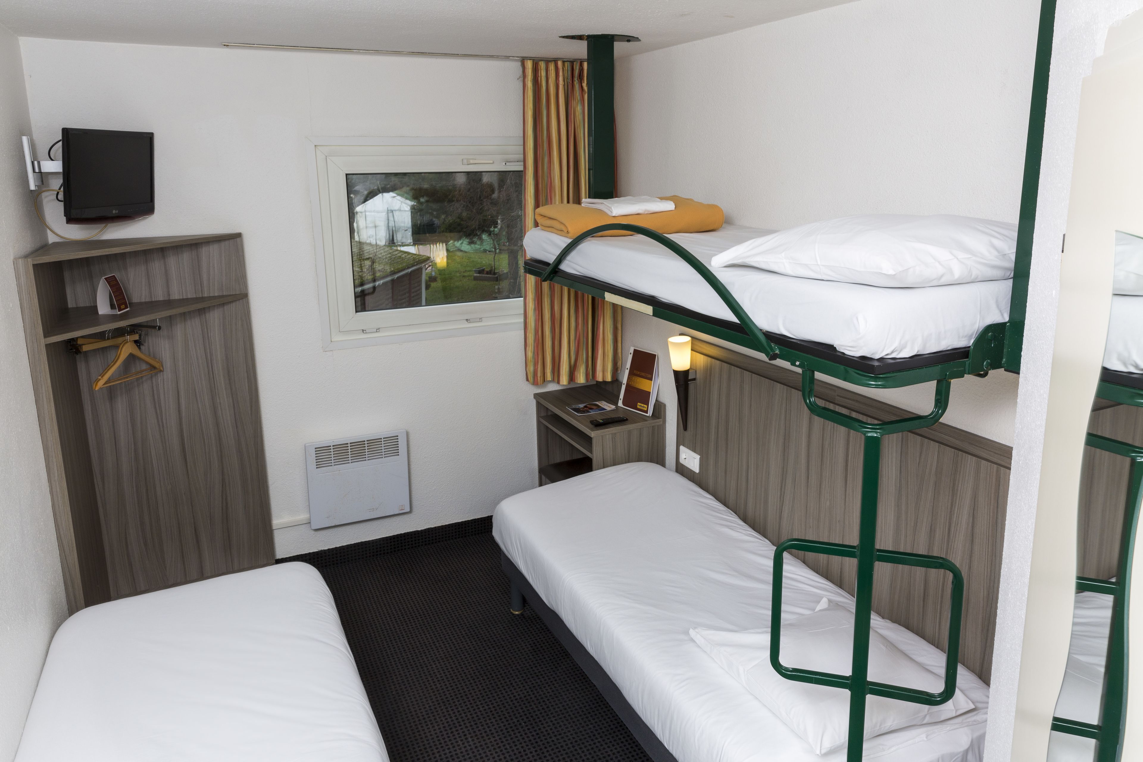 Una habitación de hotel con literas, televisor, ventana con cortinas, escritorio con silla y calefacción.