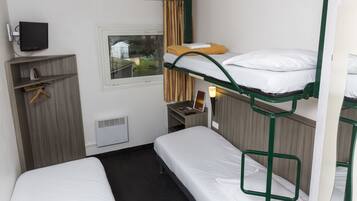 Una habitación de hotel con literas, televisor, ventana con cortinas, escritorio con silla y calefacción.