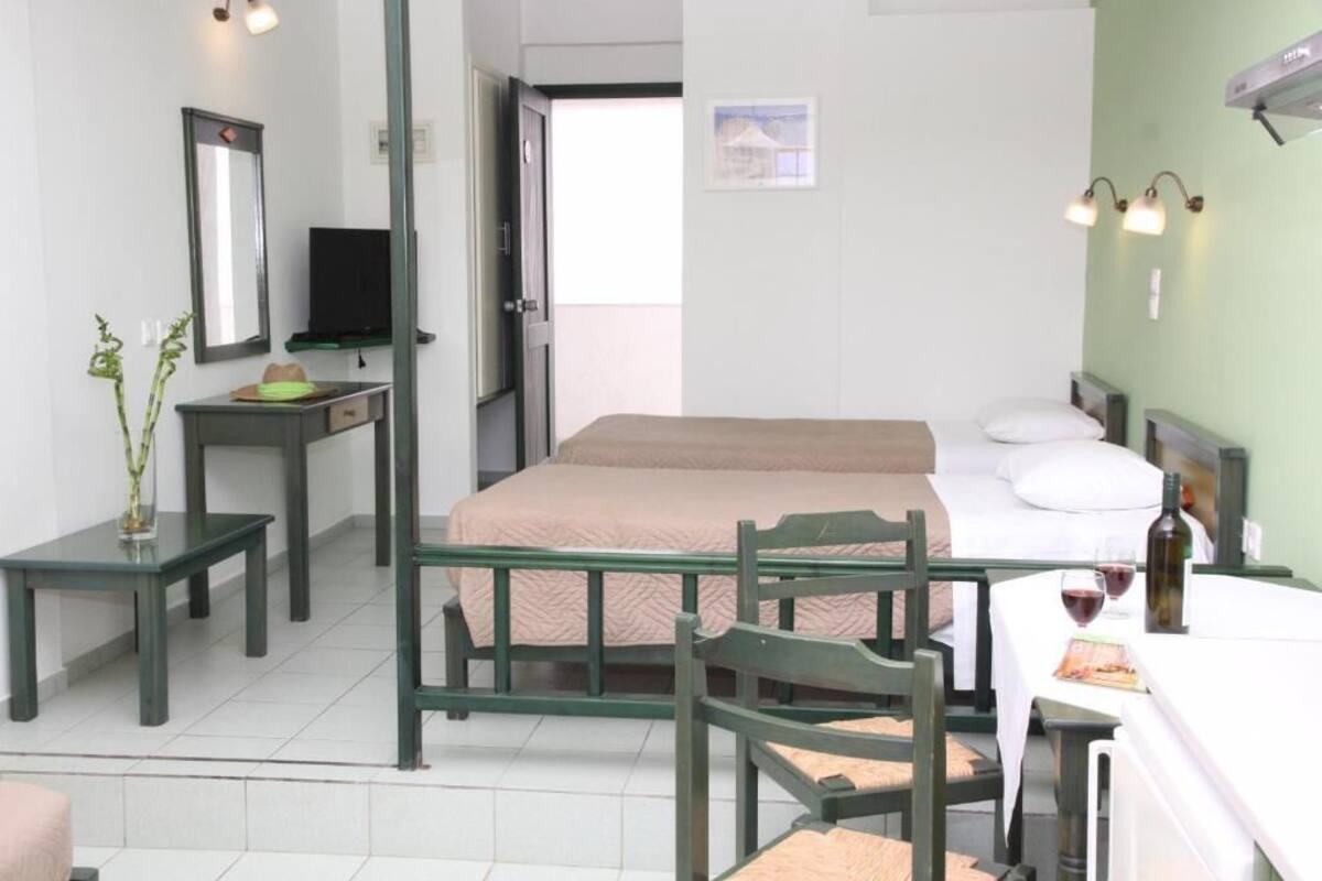 Un dormitorio con una cama, un escritorio, sillas, un televisor y una mesa con una botella y vasos.