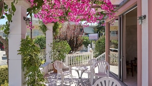 An outdoor patio with white plastic chairs and tables, surrounded by potted plants and flowering bougainvillea. - Apollon Hotel Apartments (Rethymno)
