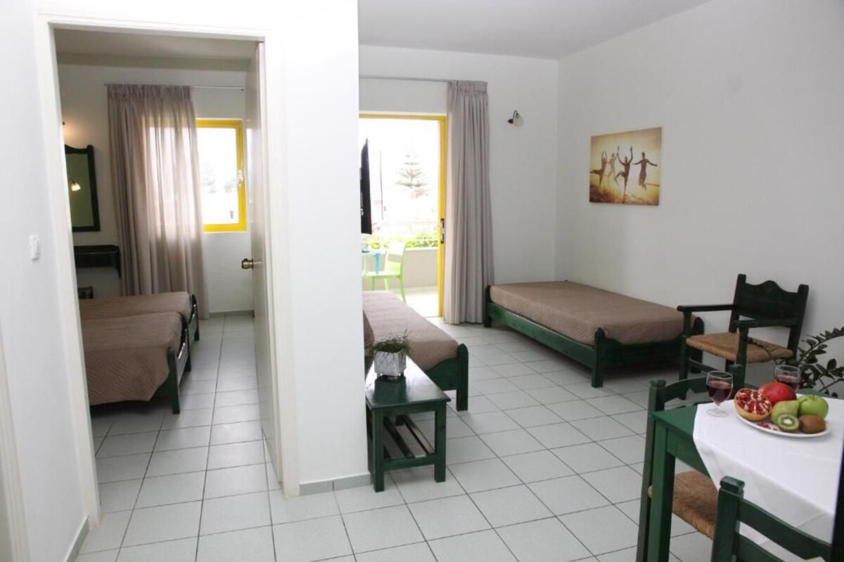 A room with two single beds, a small table with a fruit bowl, and a chair.