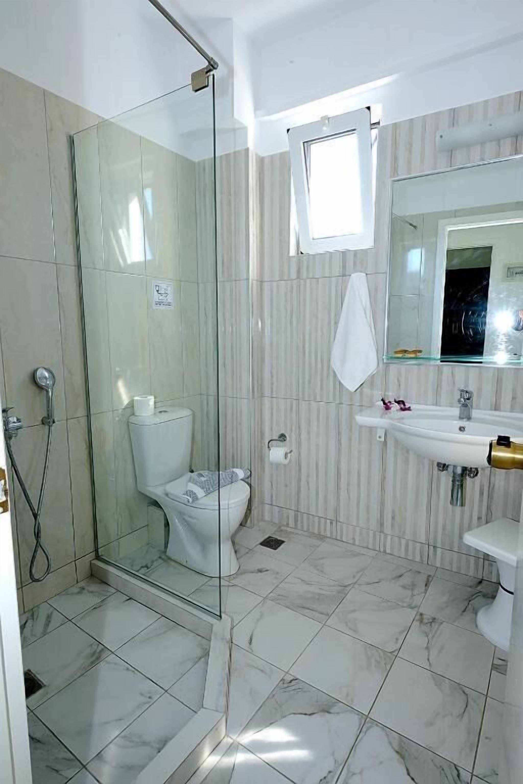 A bathroom with a glass shower enclosure, a toilet, a sink, and a mirror.