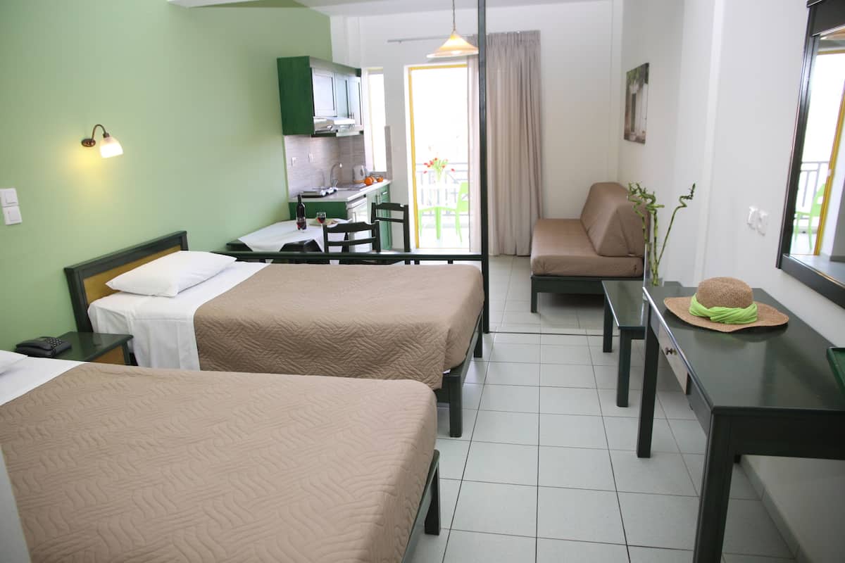 Habitación de hotel con dos camas, una mesa de comedor, una silla, un sofá, una mesita con un sombrero y un balcón con vistas.