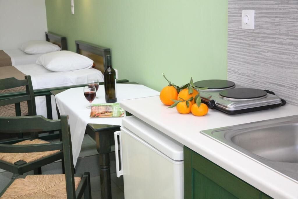 A small kitchenette with a sink, a wine bottle, and a fruit bowl containing oranges.