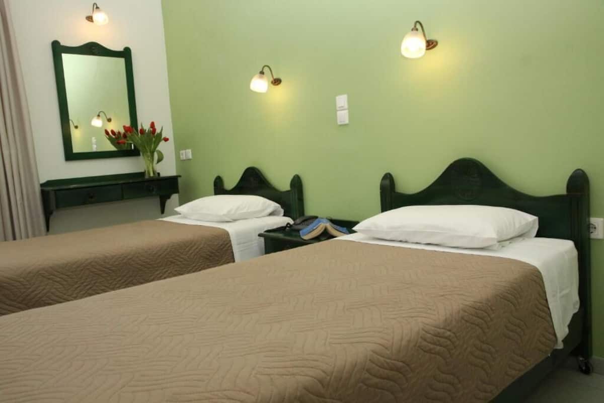 Una habitación de hotel con dos camas individuales, una pared verde, un espejo y lámparas de noche.