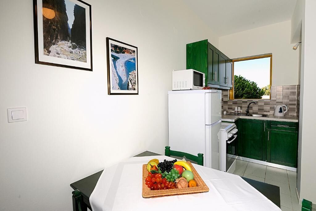 A small room with a bed, a table with fruit, a microwave, and a view of a green landscape.