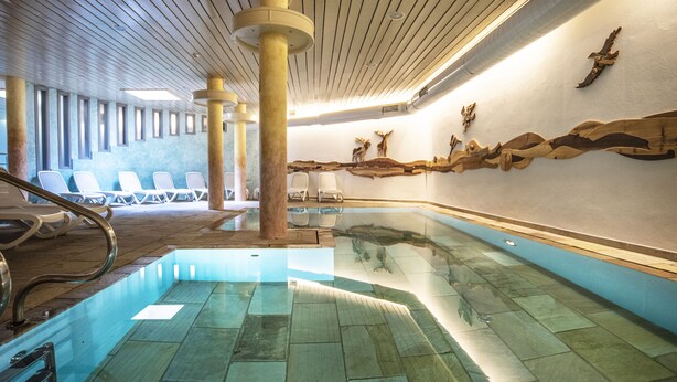 A swimming pool with clear water, surrounded by lounge chairs and wooden pillars. - Al Sole Clubresidence (Canazei)