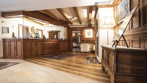 A spacious room with wooden floors, a reception desk, a white chair, and a painting on the wall. - Al Sole Clubresidence (Canazei)