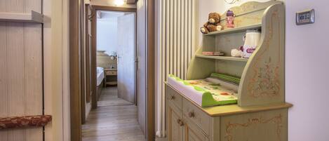 A narrow hallway with a wooden floor, a green and white cabinet with a teddy bear, and a radiator on the wall.