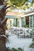 Ein Außenbereich mit Terrasse, Tischen und Stühlen, umgeben von Blumentöpfen und einem Gebäude mit großen Fenstern.