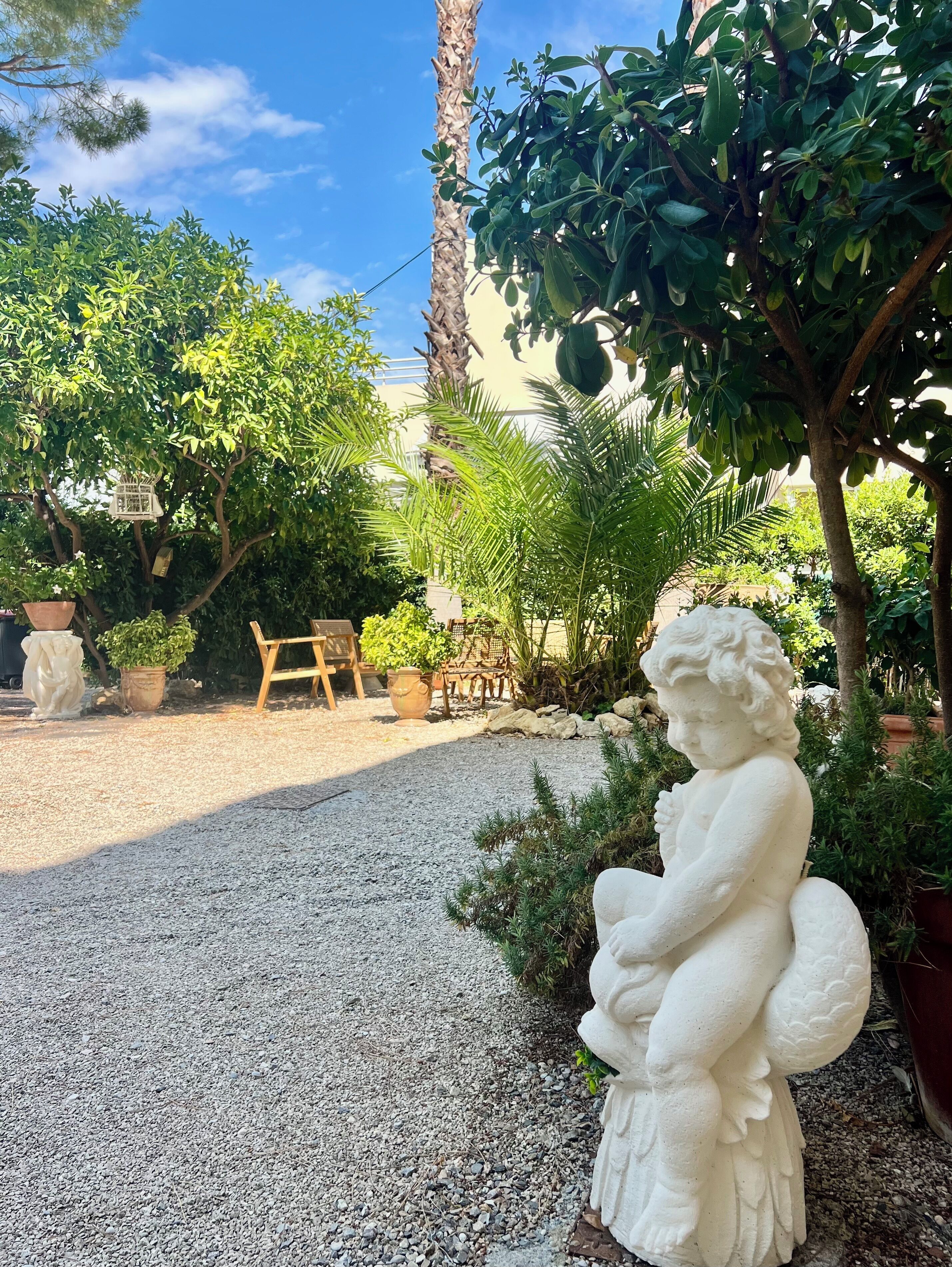 Un jardín con una estatua, un sendero de grava y plantas en macetas.