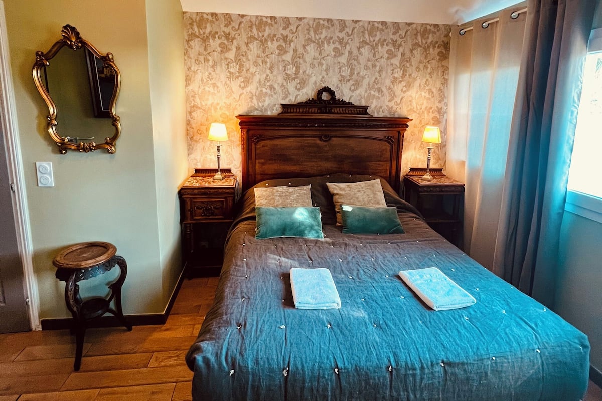 Ein Schlafzimmer mit einem großen Bett, zwei Nachttischlampen, einem Spiegel und einer Deckenleuchte.